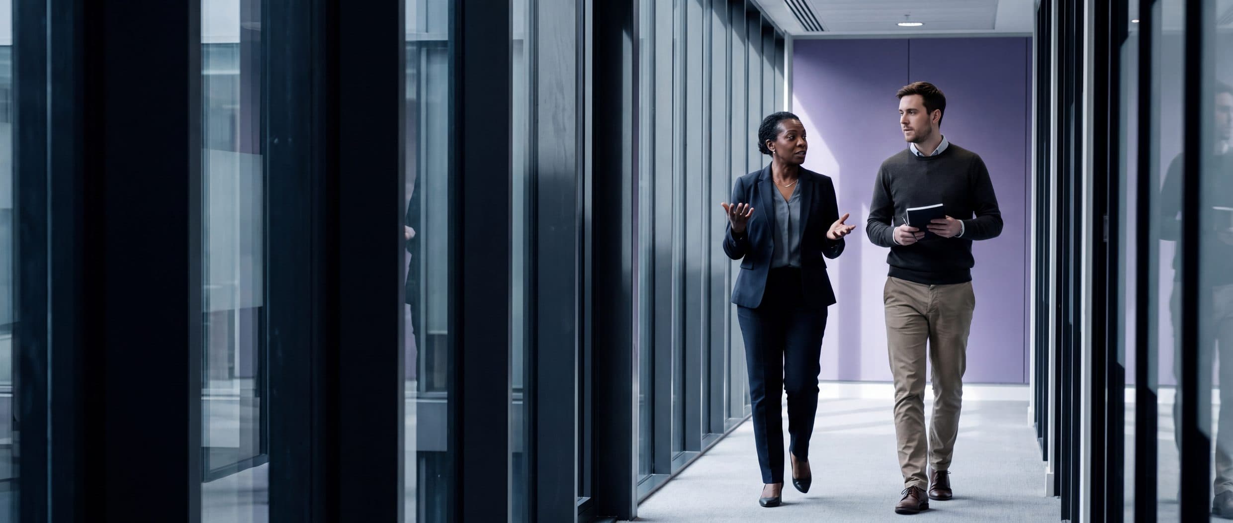 Two senior leaders in conversation walking down a glazed office corridor